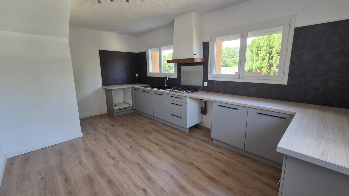 Cuisine moderne et spacieuse d'une maison à Saint-Aunès, avec des meubles gris et un plan de travail en bois.