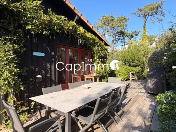Terrace of a villa in Lège-Cap-Ferret with table and chairs, surrounded by greenery.