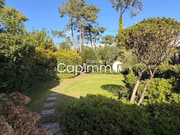 Lush garden of a villa in Lège-Cap-Ferret with stone path and trees.