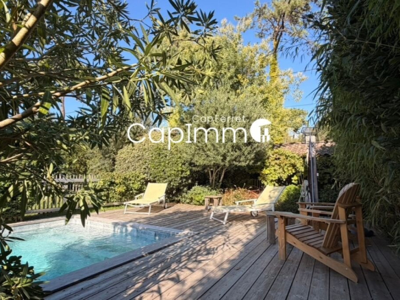 Wooden terrace with sun loungers and swimming pool, surrounded by greenery in a villa in Lège-Cap-Ferret.