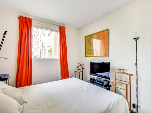 Chambre lumineuse avec rideaux orange et télévision, vue sur l'extérieur.