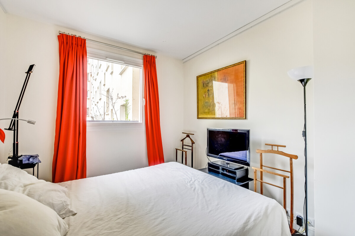 Chambre rénovée à Paris 15ème Chambre lumineuse avec rideaux orange et télévision, vue sur l'extérieur.
