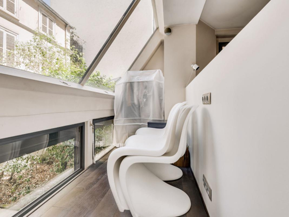 Intérieur d'un duplex à Paris avec des chaises blanches et une vue sur un espace extérieur.