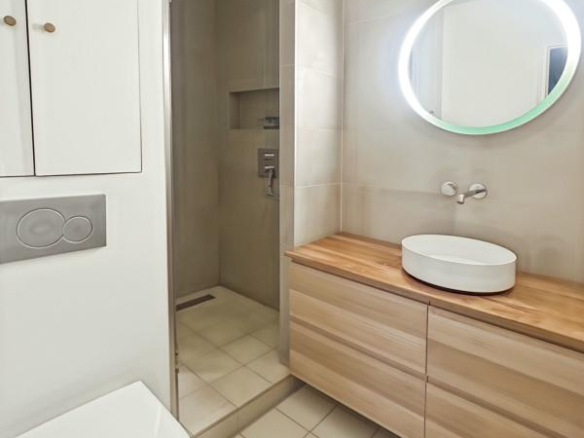 Modern bathroom with shower, wooden vanity unit and round mirror.