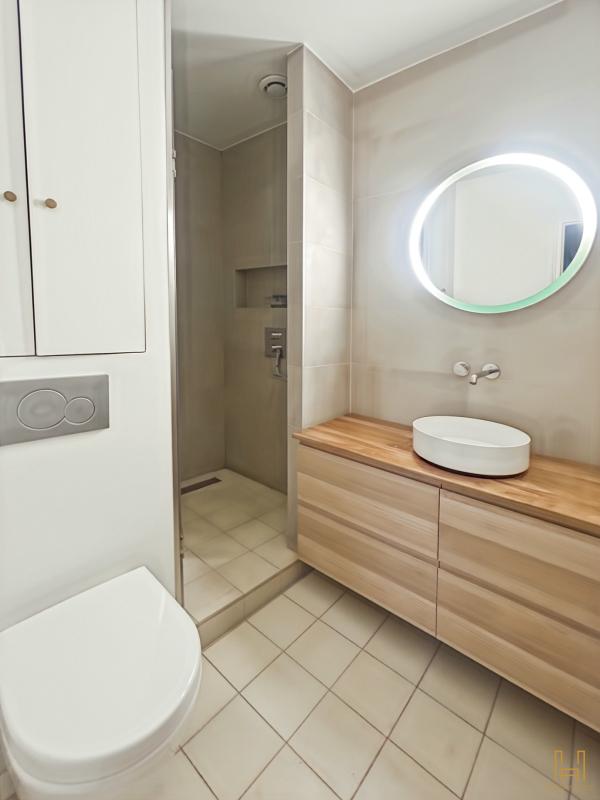 Bathroom of an apartment in the 9th arrondissement of Paris Modern bathroom with shower, wooden vanity unit and round mirror.
