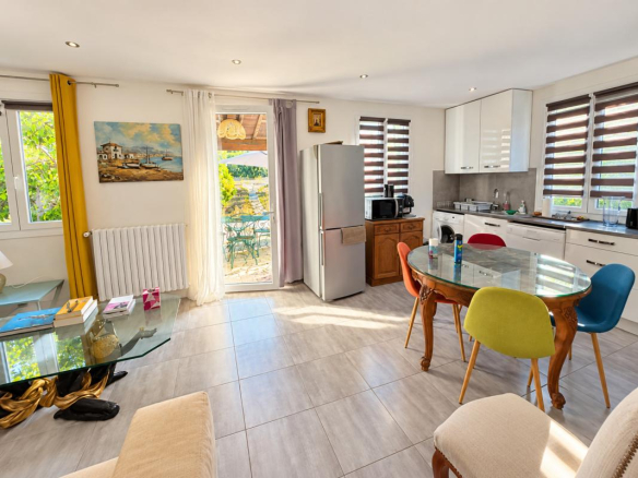 Intérieur d'une maison avec salon, cuisine équipée et salle à manger, vue sur la nature.
