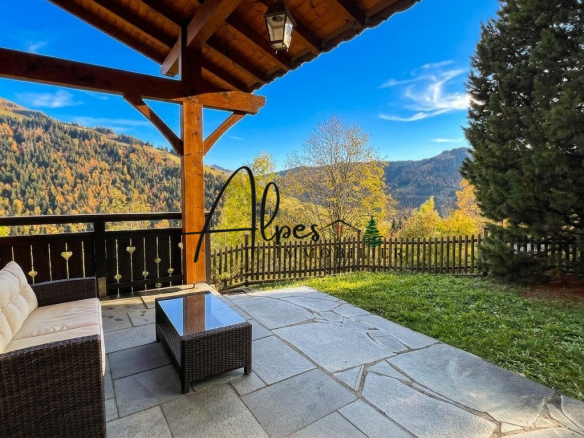 Terrasse d'un chalet avec vue sur les montagnes à La Clusaz, entourée d'arbres.