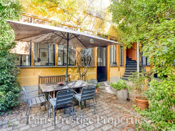 Jardin d'un ancien atelier d'artiste à Paris 11ème avec table et chaises sous un parasol.