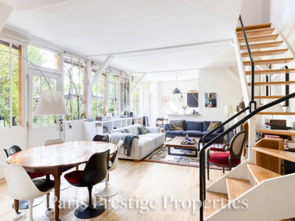 Intérieur d'un ancien atelier d'artiste à Paris, avec salon, salle à manger et jardin visible.