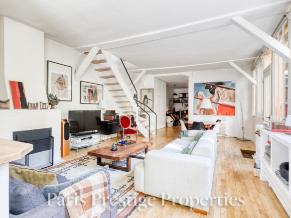 Intérieur d'un ancien atelier d'artiste à Paris, avec un salon lumineux et un escalier en bois.