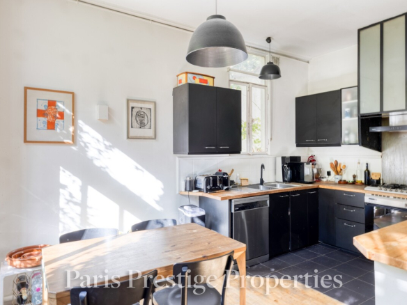Cuisine moderne avec meubles noirs et plan de travail en bois dans un ancien atelier d'artiste à Paris.