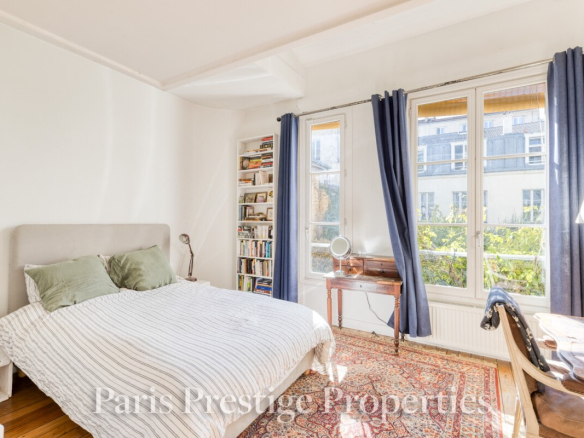 Chambre lumineuse avec lit double, bibliothèque et bureau, fenêtres donnant sur un jardin.