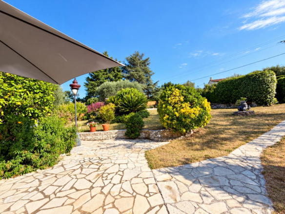 Jardin arboré avec chemin en pierre et parasol, vue dégagée sur la nature.