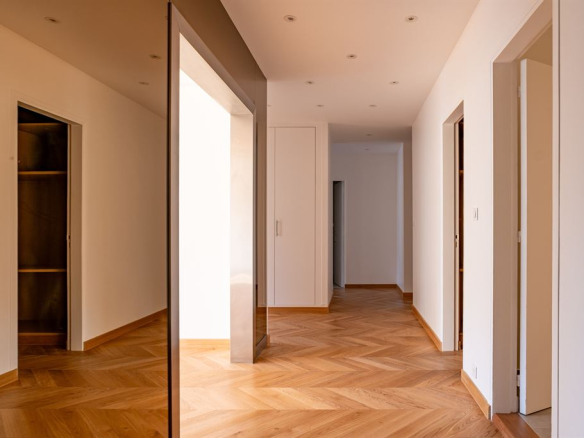 Interior of a renovated apartment with parquet flooring and light walls, view of a hallway.