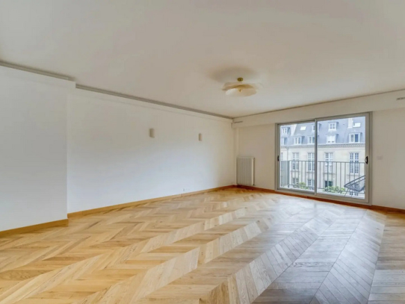 Interior of a renovated apartment with parquet flooring, windows overlooking a balcony and gardens.