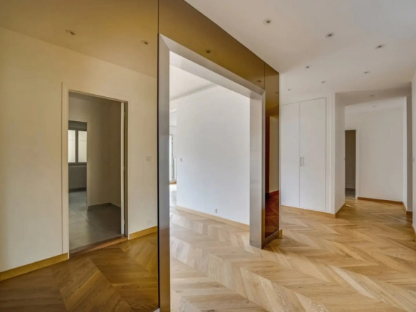 Interior of a renovated apartment with herringbone parquet flooring and light walls, view of a corridor.