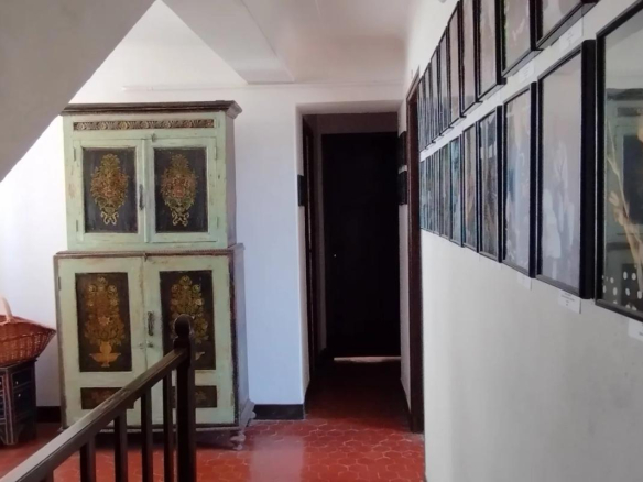 Intérieur d'une ancienne auberge avec des cadres accrochés au mur et un meuble ancien.