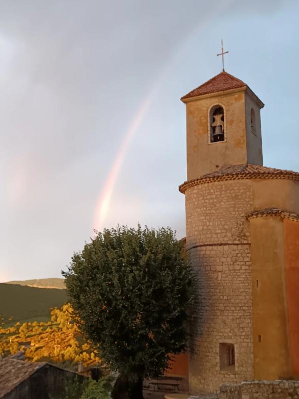 Église de Coursegoules Église avec clocher et arbre, sous un ciel partiellement nuageux avec un arc-en-ciel à Coursegoules.