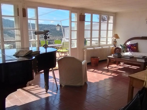 Intérieur lumineux d'une ancienne auberge à Coursegoules avec piano et vue sur la nature.