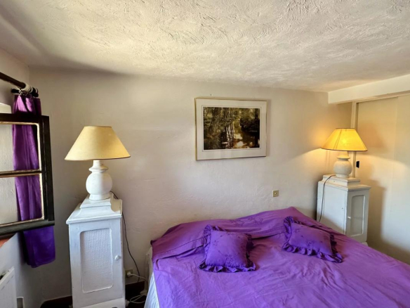 Chambre d'une villa avec lit double et lampes de chevet, fenêtres et décoration simple.