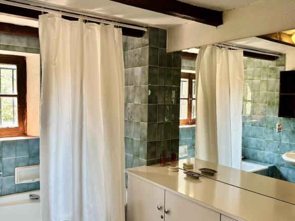 Salle de bain d'une villa avec carrelage bleu et miroir, fenêtres en bois.