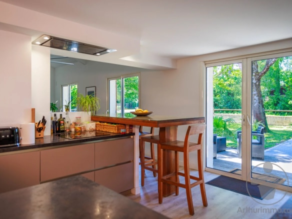 Intérieur d'une maison moderne avec cuisine ouverte et bar, vue sur le jardin.
