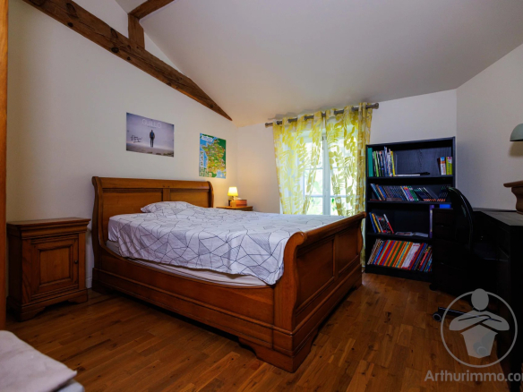Bedroom in a house with a wooden bed, desk and shelves, decorated in a simple style.