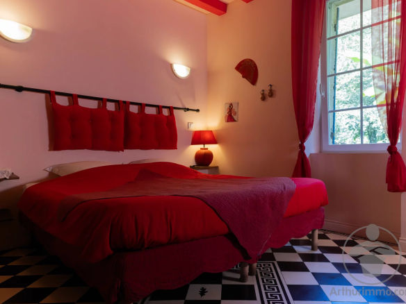 Room with double bed and red decor, windows overlooking the garden.