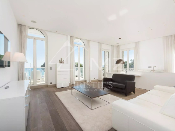 Bright open-concept living room with white furniture, large glass doors to a balcony and an ocean view.