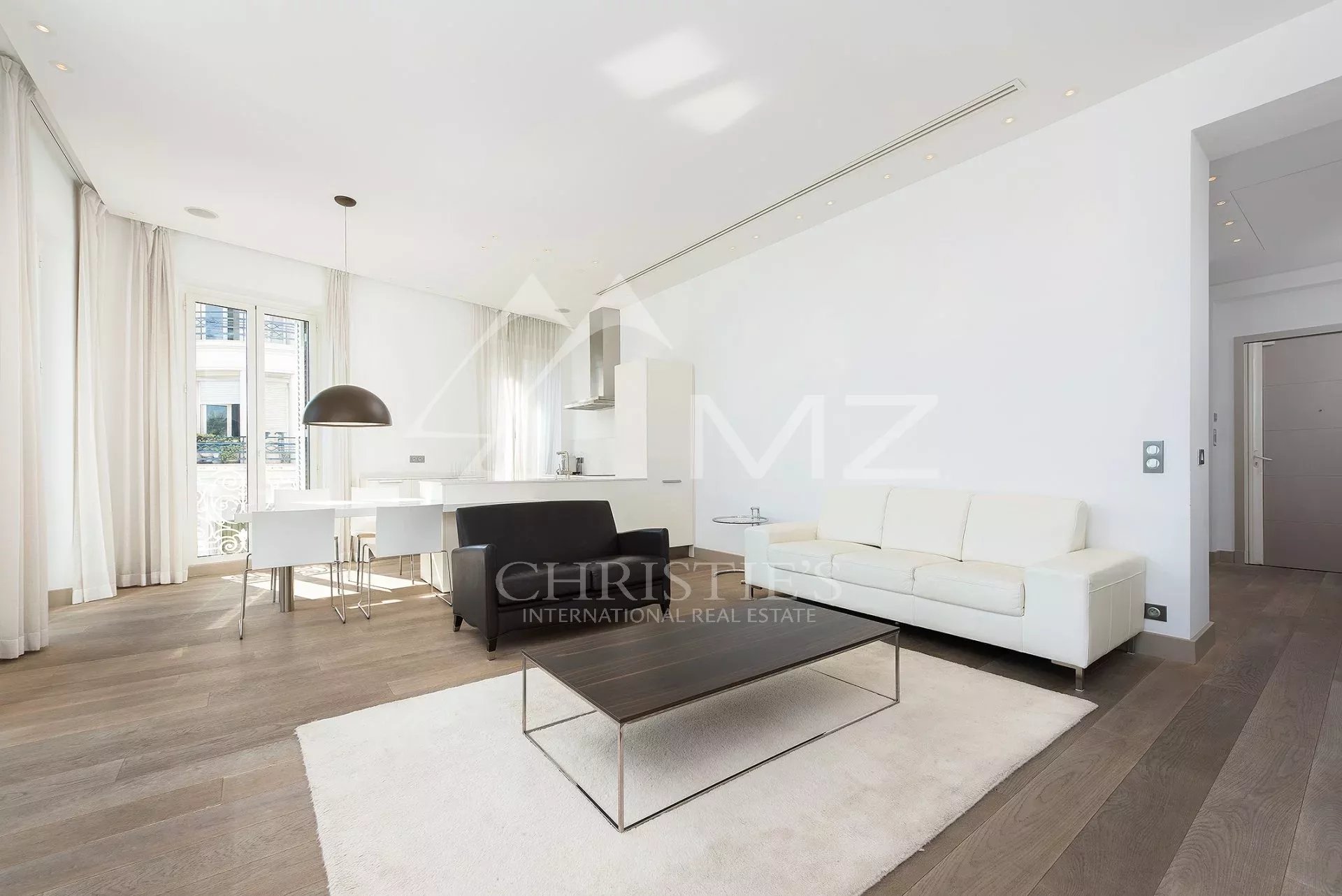 Bright open-plan living room with white sofa, black armchair, and minimalist coffee table on a cream rug