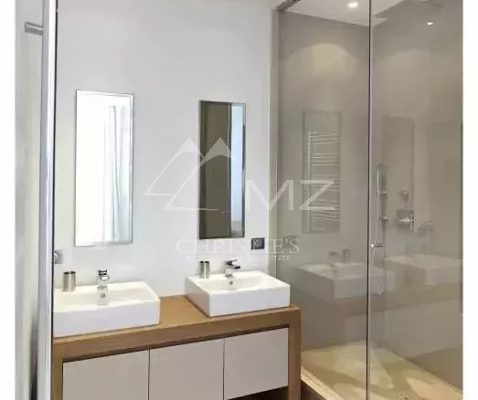 Modern bathroom with a wooden double-sink vanity, two square white sinks, mirrors, and a glass-enclosed shower.