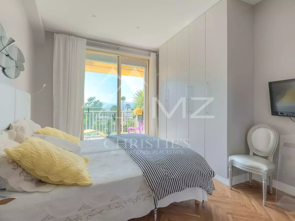 Bright bedroom with a balcony view, featuring a white bed, yellow pillows, and a striped throw blanket.