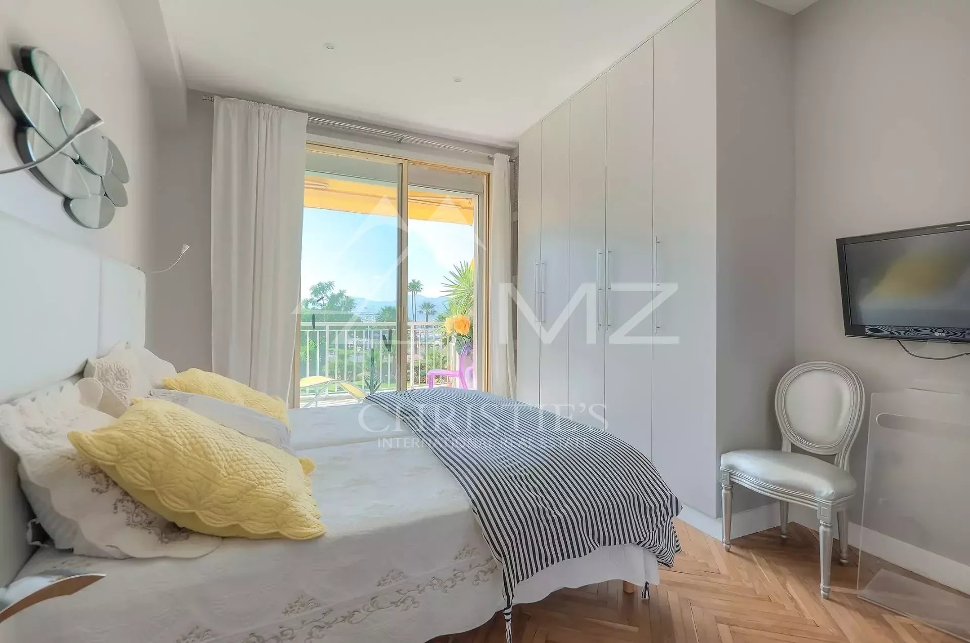 Bright bedroom with a balcony view, featuring a white bed, yellow pillows, and a striped throw blanket.