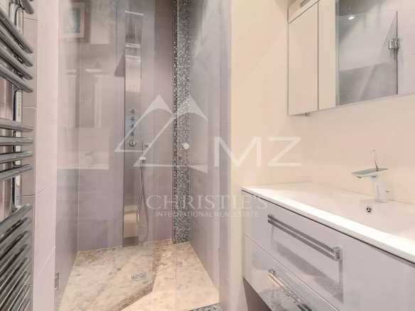 Modern bathroom with a glass shower enclosure, mosaic tile accent, and white vanity with sink and mirror cabinet.