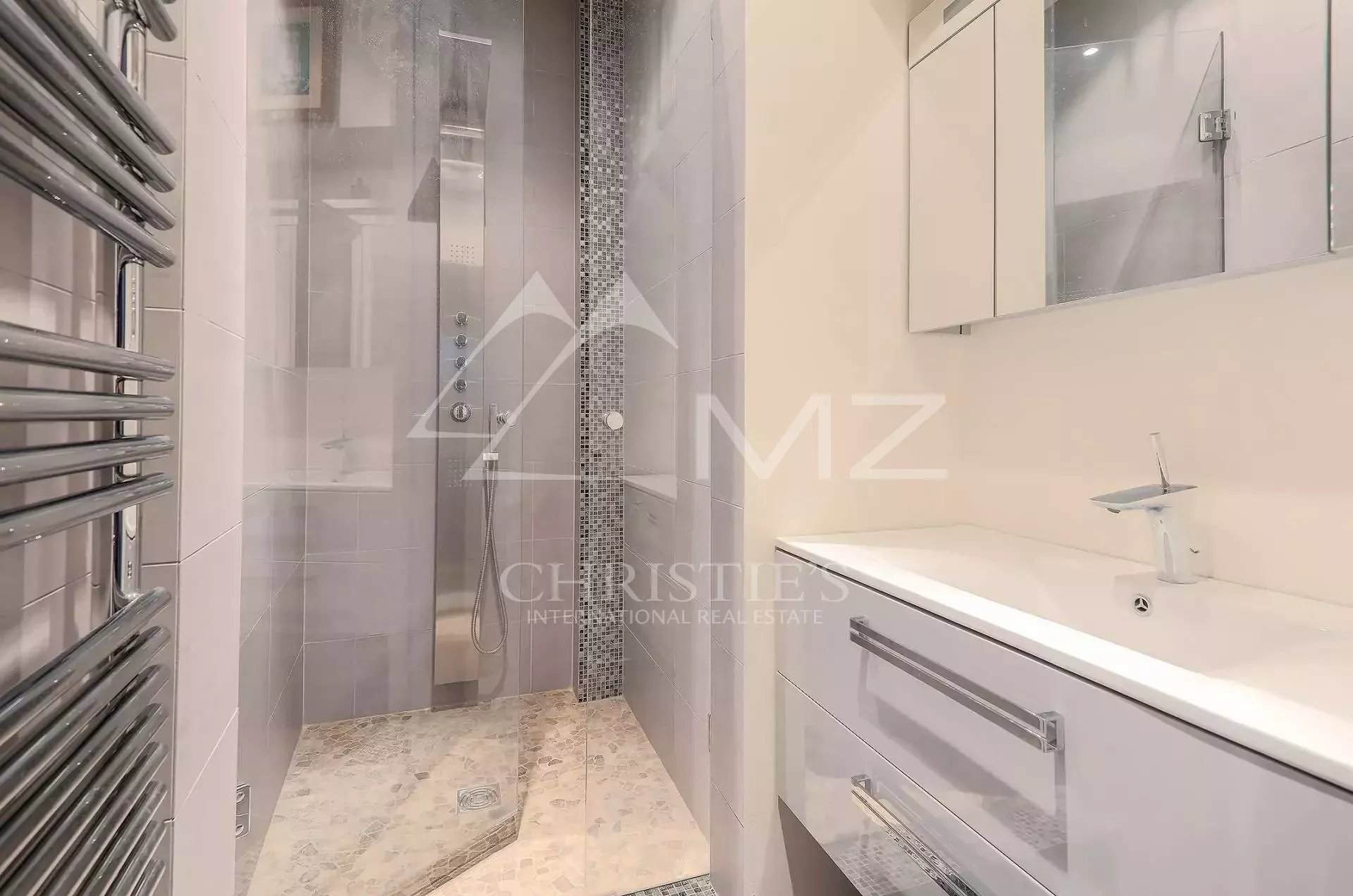 Modern bathroom with a glass shower enclosure, mosaic tile accent, and white vanity with sink and mirror cabinet.