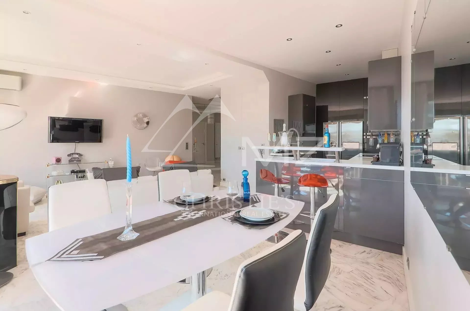 Open-concept kitchen and dining area with white table, gray cabinets, and red bar stools; modern, bright space with marble floor and minimalist decor.