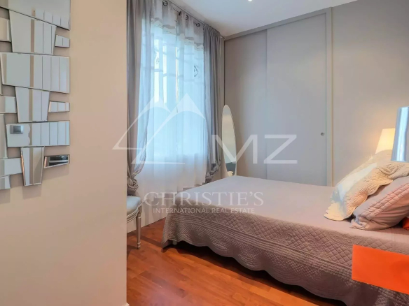Modern bedroom with a gray quilted bed, several pillows, a chrome lamp on an orange mat, and a large gray wardrobe.