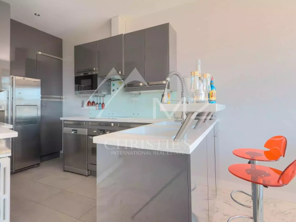 Modern kitchen with gray high-gloss cabinets, stainless steel fridge and built-in oven/m microwave, and a white island with a sink.