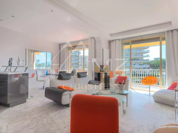 Bright, modern living area with white and orange furniture, marble floor, and large windows overlooking a urban view.