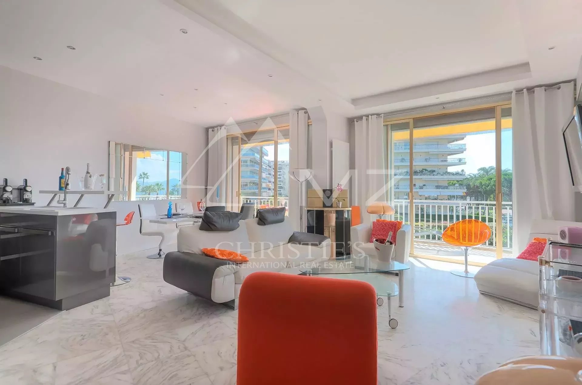 Bright, modern living area with white and orange furniture, marble floor, and large windows overlooking a urban view.