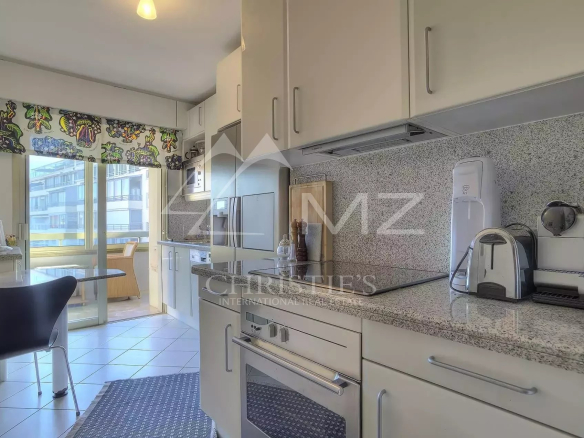 Bright kitchen with white cabinets, granite counters, and stainless appliances leading to a balcony dining area.