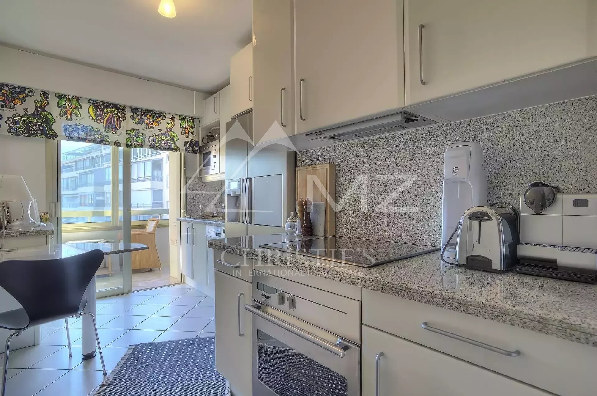Bright kitchen with white cabinets, granite counters, and stainless appliances leading to a balcony dining area.