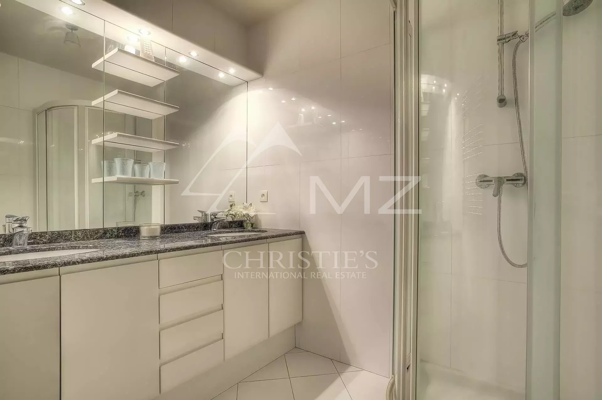 Modern white bathroom with a granite countertop vanity, large mirror, and glass shower enclosure on the right.