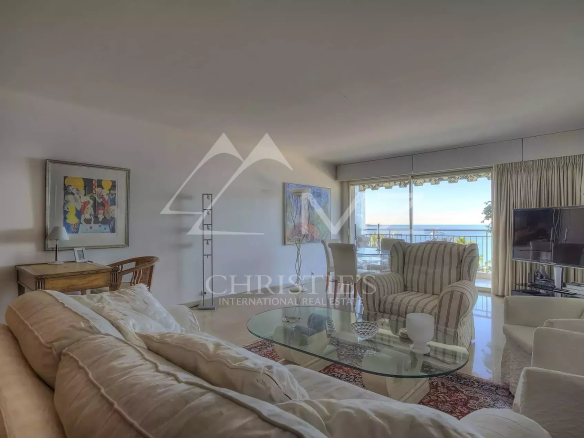 Bright living room with beige sofas, glass coffee table, and a balcony sea view through large sliding doors.