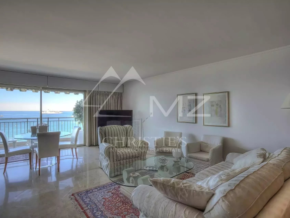 Bright living room with cream sofas, glass coffee table, and a wall of windows overlooking the ocean and balcony.