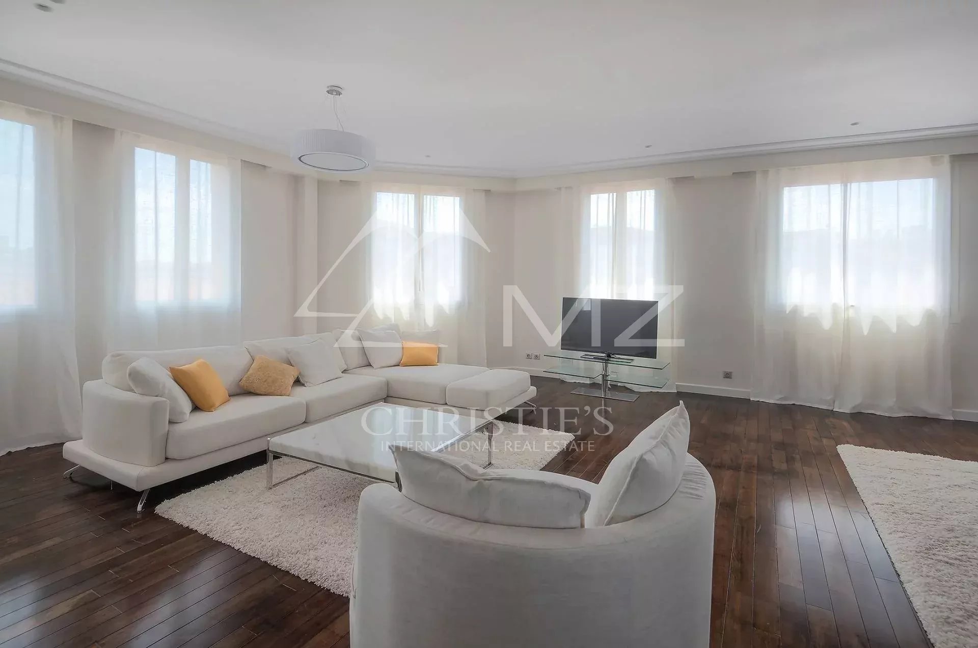 Bright living room with a white sectional sofa, coordinating cushions, glass coffee table, and a flat-screen TV on a glass stand.