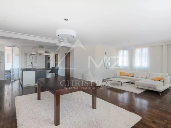 Open-plan living area with a white sectional sofa, dark wood dining table, and a modern kitchen; large windows brighten the space.