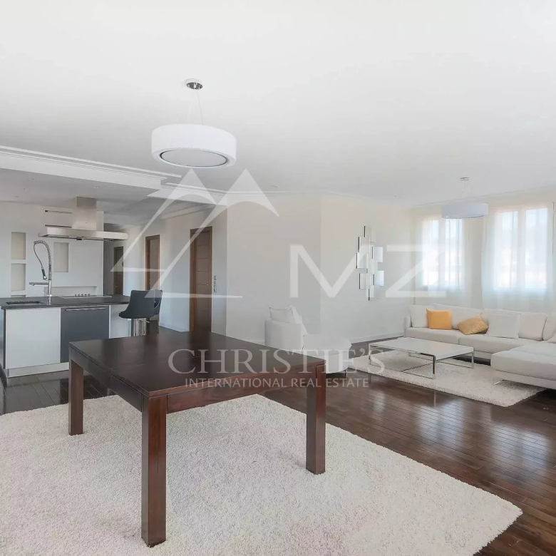 Open-plan living area with a white sectional sofa, dark wood dining table, and a modern kitchen; large windows brighten the space.