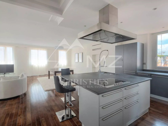 Open-concept kitchen with a stainless steel island, built-in cooktop and large range hood, dark cabinets, and a living area with white seating nearby.