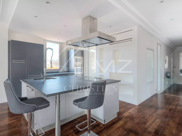 Modern kitchen with a large island, gray bar stools, and stainless steel appliances in a bright, open space.
